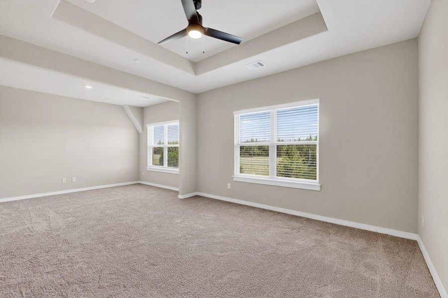 Empty room with a tray ceiling, light colored carpet, and ceiling fan Empty room with a tray ceiling, light colored carpet, and ceiling fan