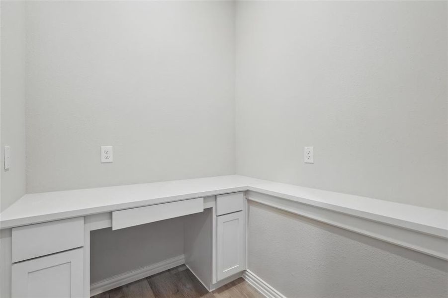 Unfurnished office with built in study area, wood finished floors, and baseboards