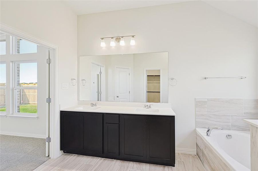 Bathroom with vanity, a relaxing tiled tub, and lofted ceiling