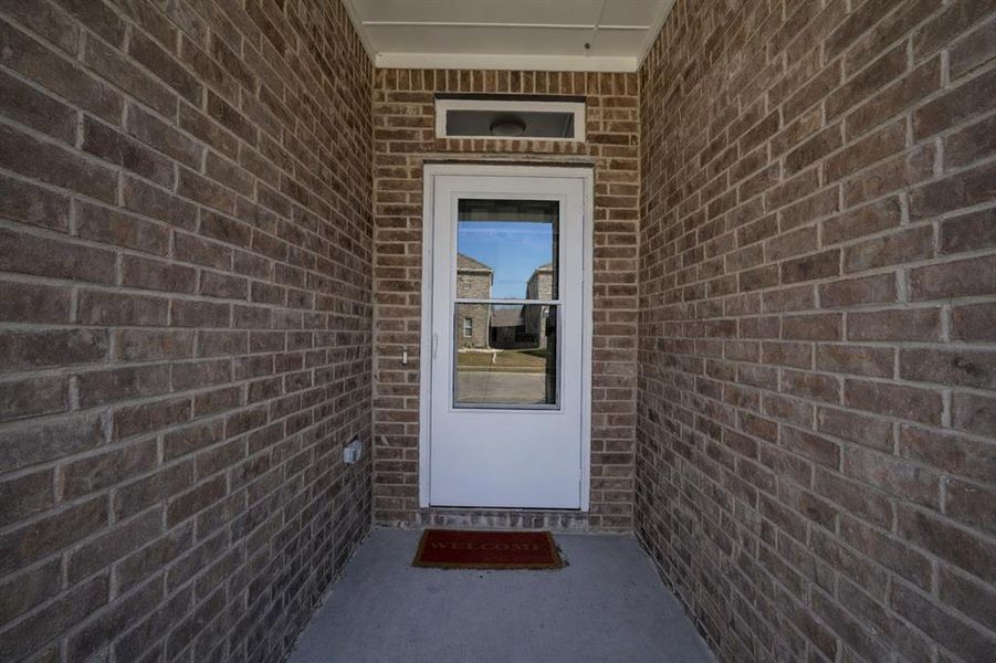 Covered entryway featuring a white storm door, transom window, and brick facade