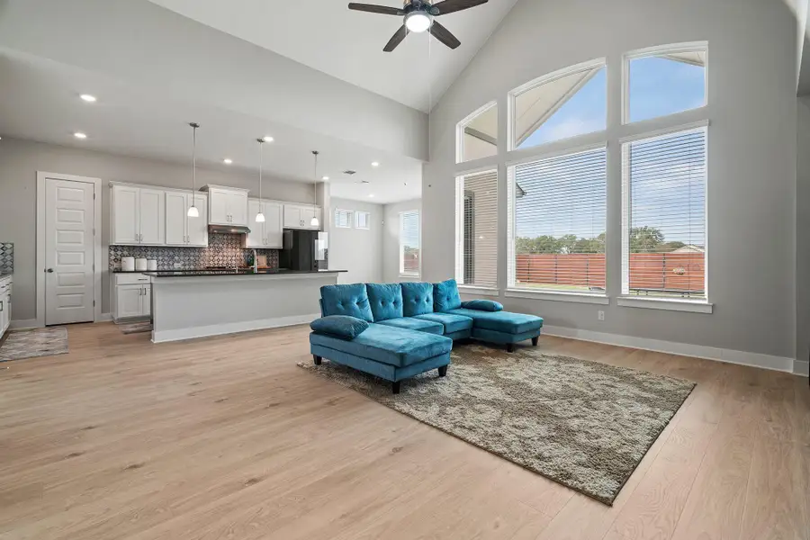 Living area with high vaulted ceiling, light wood-style flooring, plenty of natural light, and a ceiling fan Living area with high vaulted ceiling, light wood-style flooring, plenty of natural light, and a ceiling fan