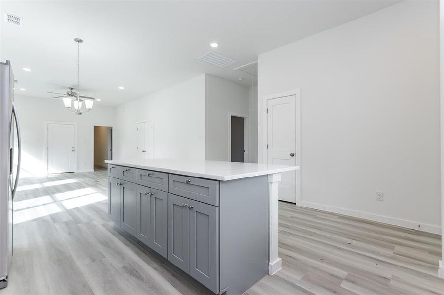 Kitchen featuring a center island, gray cabinetry, ceiling fan, stainless steel refrigerator, and light hardwood / wood-style flooring