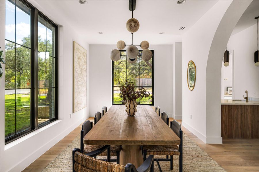 Natural light floods this inviting dining space, featuring elegant arched doorways and gleaming hardwood floors.