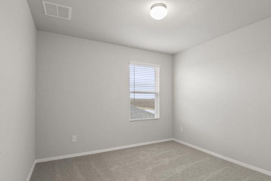 Image of a bedroom with tan carpeting and light grey walls with a window