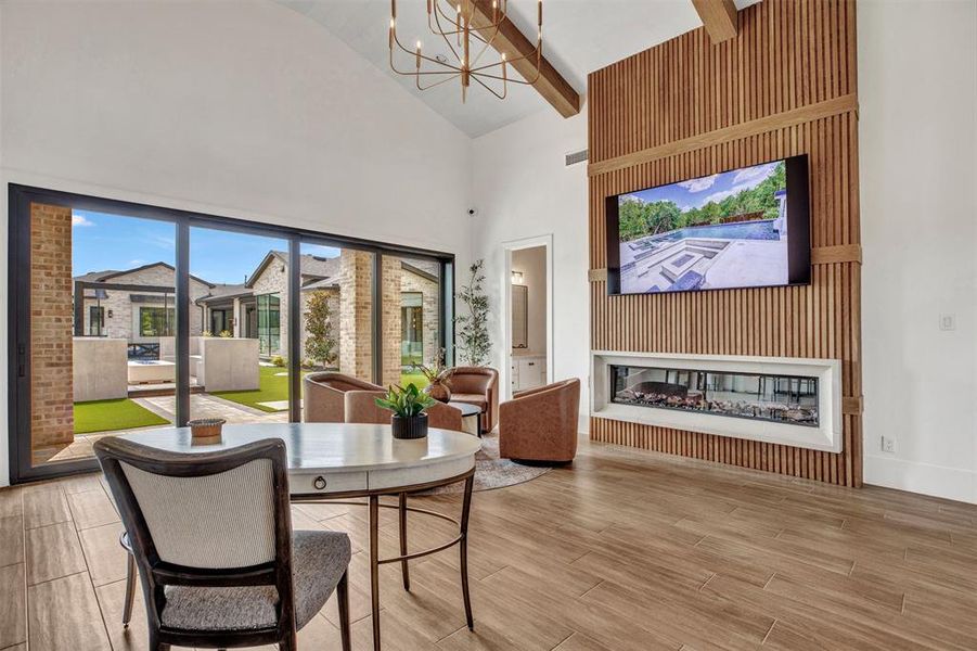 Dining space featuring a chandelier, high vaulted ceiling, wood finish floors, a glass covered fireplace, and beam ceiling Dining space featuring a chandelier, high vaulted ceiling, wood finish floors, a glass covered fireplace, and beam ceiling