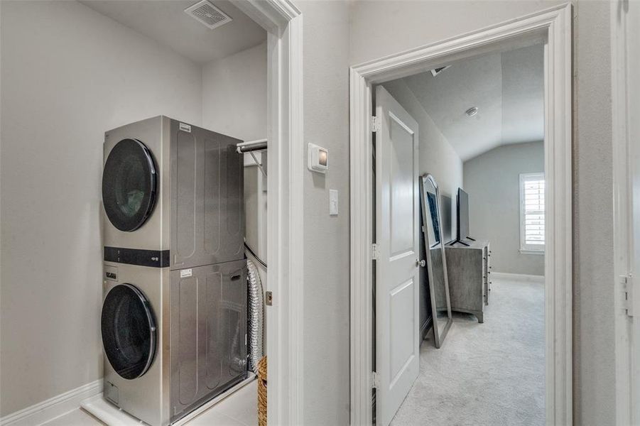 Clothes washing area with light carpet and stacked washer and dryer