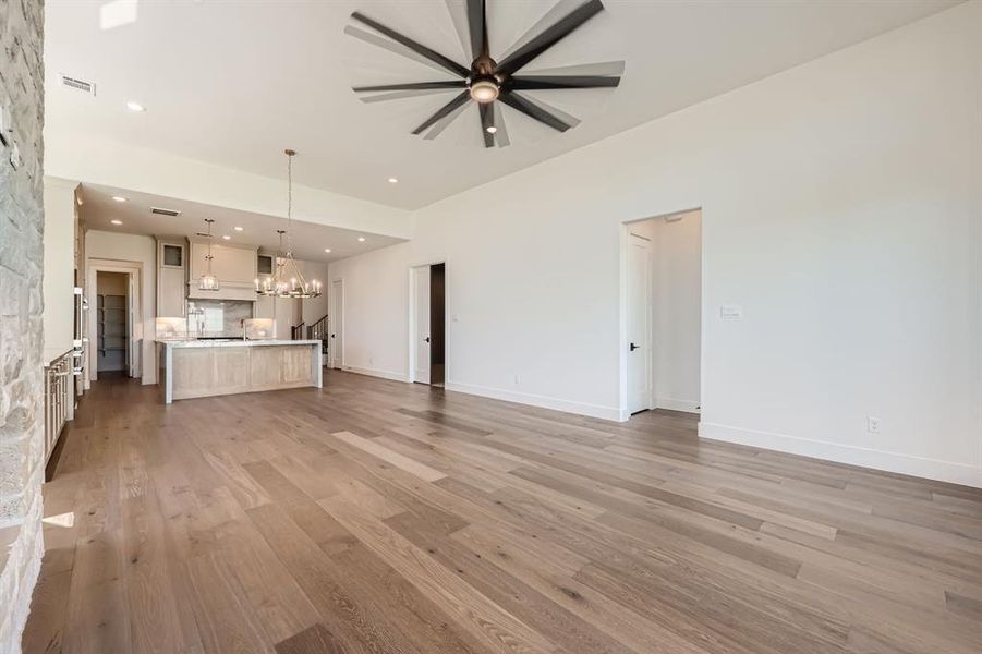 Unfurnished living room featuring ceiling fan with notable chandelier and light wood-type flooring