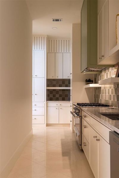 Kitchen featuring stainless steel appliances, light stone countertops, decorative backsplash, light tile patterned floors, and white cabinets