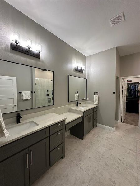 Bathroom with a spacious closet, two vanities, a tile shower, and light tile patterned floors
