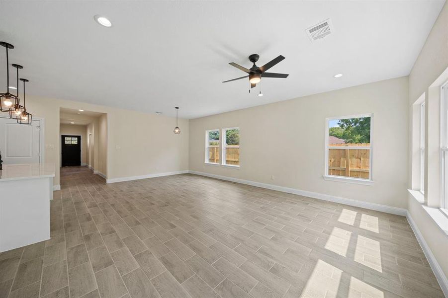 Unfurnished living room featuring ceiling fan with notable chandelier, plenty of natural light, and light hardwood / wood-style floors