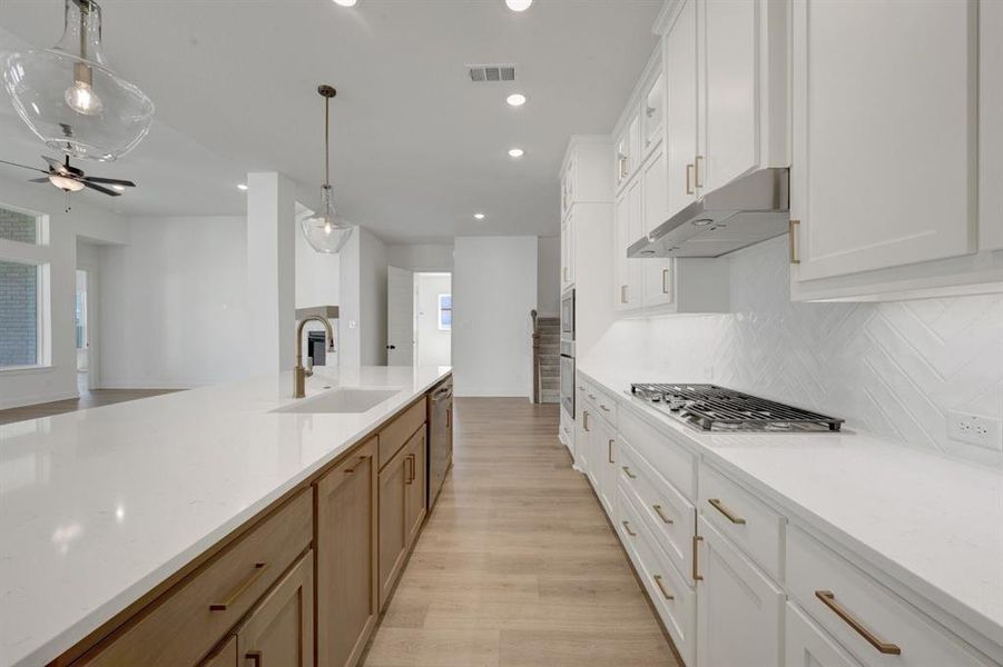 Modern kitchen featuring a spacious island with an undermount sink and brass faucet, white perimeter cabinetry with brass hardware, a built-in gas cooktop, and a white herringbone tile backsplash