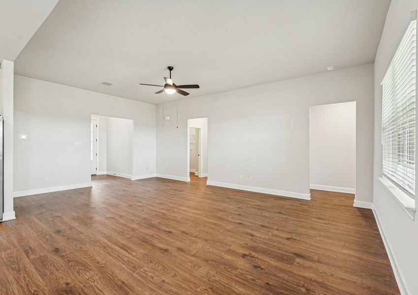 Open-concept family room featuring a ceiling fan, wood-look vinyl flooring, and a sightline into the kitchen and dining area. Open-concept family room featuring a ceiling fan, wood-look vinyl flooring, and a sightline into the kitchen and dining area.