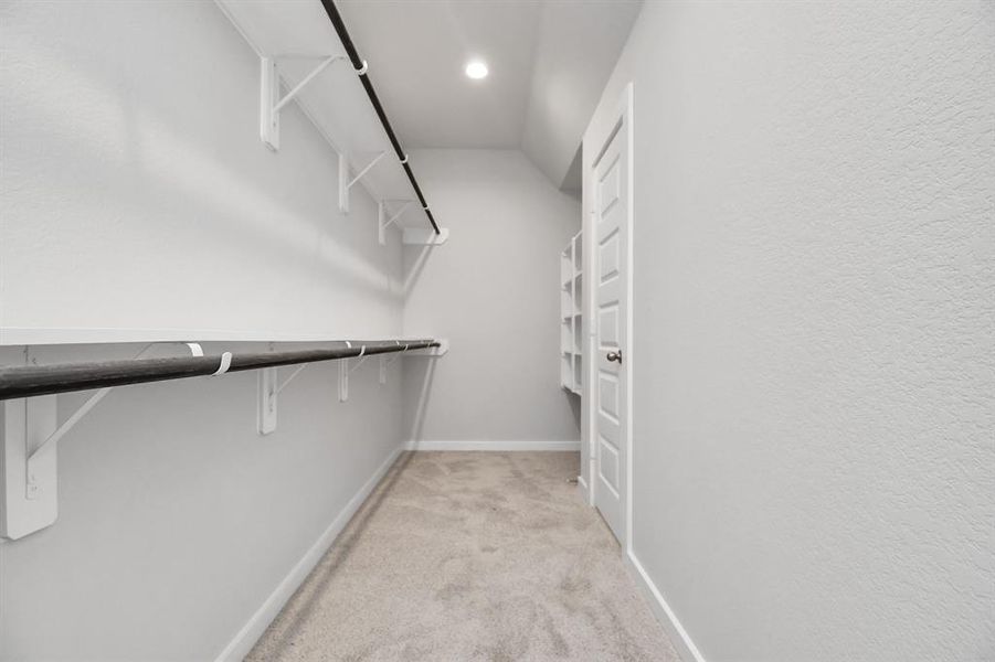 Spacious walk-in closet with high ceilings, plush carpet, and recessed lighting. Warm paint tones, built-in shelving, and dark finishes create a contemporary and functional retreat. Sample photo of completed home with similar floor plan. Actual colors and selections may vary.