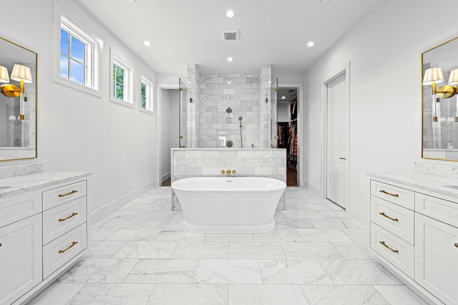 A spa-like retreat, the primary bath features dual vanities w/ honed marble countertops, abundant storage & Visual Comfort sconces. A freestanding soaking tub creates a striking focal point, while elevated finishes throughout enhance the overall experience. Doors to the left and right of the shower lead to the massive walk-in closet A spa-like retreat, the primary bath features dual vanities w/ honed marble countertops, abundant storage & Visual Comfort sconces. A freestanding soaking tub creates a striking focal point, while elevated finishes throughout enhance the overall experience. Doors to the left and right of the shower lead to the massive walk-in closet