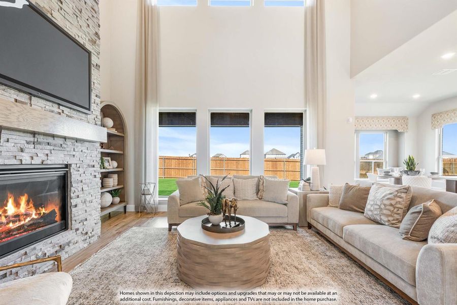Living room with two-story ceiling, stone fireplace, built-in shelves, and large windows overlooking backyard Living room with two-story ceiling, stone fireplace, built-in shelves, and large windows overlooking backyard