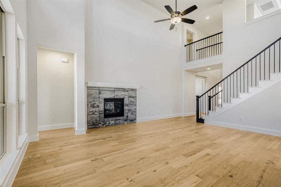 Unfurnished living room with a high ceiling, a stone fireplace, light wood-style flooring, and a ceiling fan