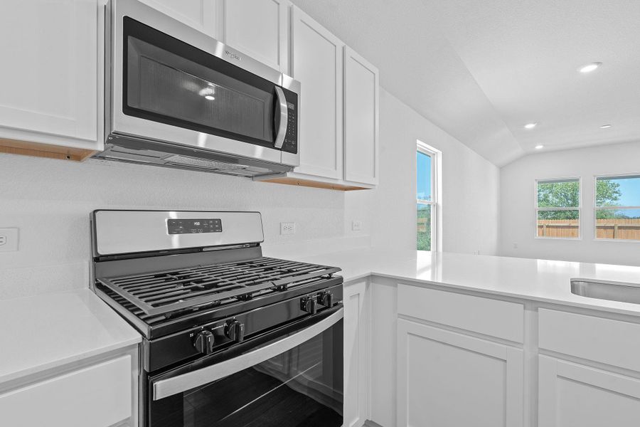 Kitchen featuring appliances with stainless steel finishes, white cabinets, recessed lighting, light stone counters, and vaulted ceiling Kitchen featuring appliances with stainless steel finishes, white cabinets, recessed lighting, light stone counters, and vaulted ceiling