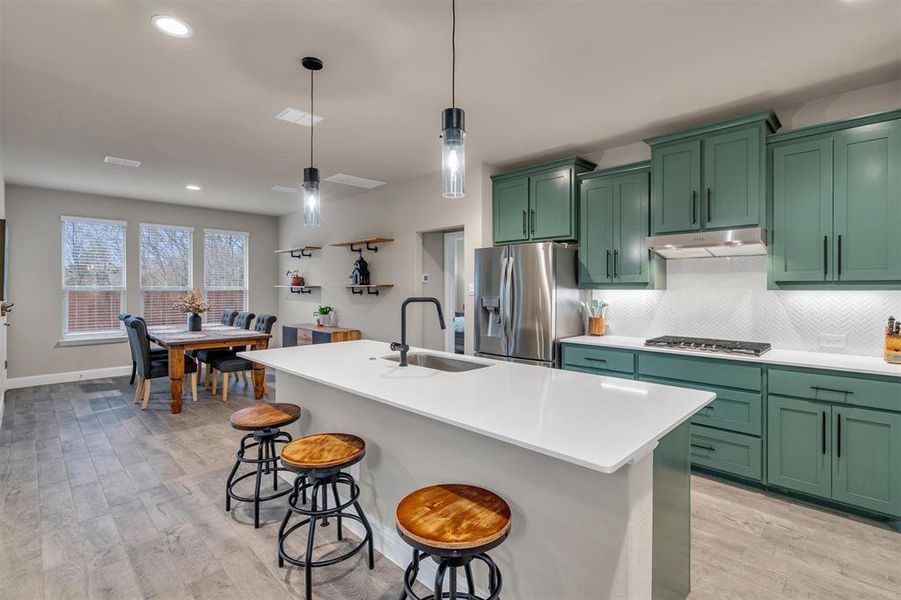 Kitchen featuring green cabinets, a breakfast bar area, decorative light fixtures, a kitchen island with sink, and light wood-style flooring