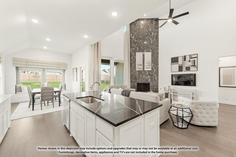 Open-concept kitchen with dark marble island, white cabinets, and tall stone fireplace in adjoining living area Open-concept kitchen with dark marble island, white cabinets, and tall stone fireplace in adjoining living area