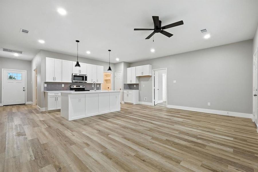 Kitchen featuring hanging light fixtures, white cabinetry, a kitchen island with sink, decorative backsplash, and light countertops Kitchen featuring hanging light fixtures, white cabinetry, a kitchen island with sink, decorative backsplash, and light countertops