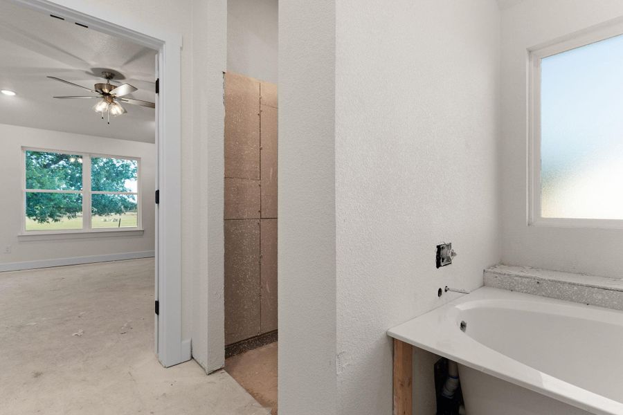 Full bath with a garden tub, plenty of natural light, concrete floors, and a ceiling fan Full bath with a garden tub, plenty of natural light, concrete floors, and a ceiling fan