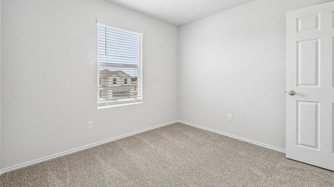 A well-lit room awaits your personal touch, featuring soft carpeting and a window offering neighborhood views.