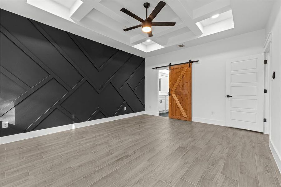 Empty room with coffered ceiling, beam ceiling, light hardwood / wood-style flooring, a barn door, and ceiling fan