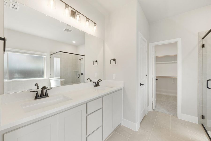 Master bathroom with double vanity, white cabinets, glass shower, and walk-in closet entrance