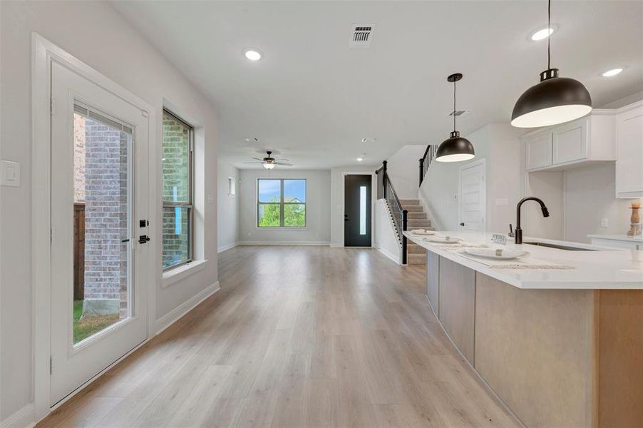 Open-concept living space featuring wood-finish flooring, recessed lighting, a modern kitchen island with pendant lighting, a built-in kitchen sink, and a staircase with dark railings