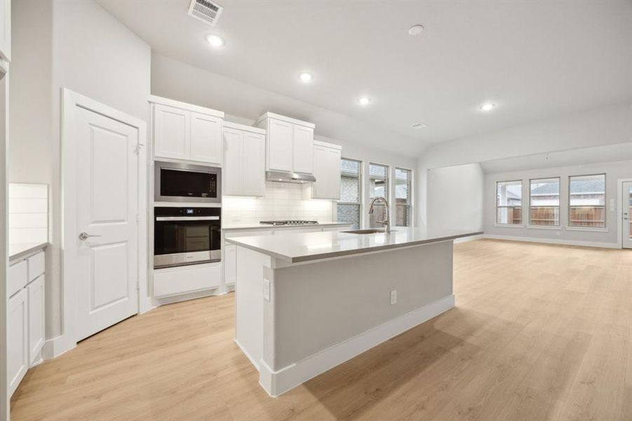 Kitchen featuring sink, appliances with stainless steel finishes, white cabinetry, tasteful backsplash, and a center island with sink