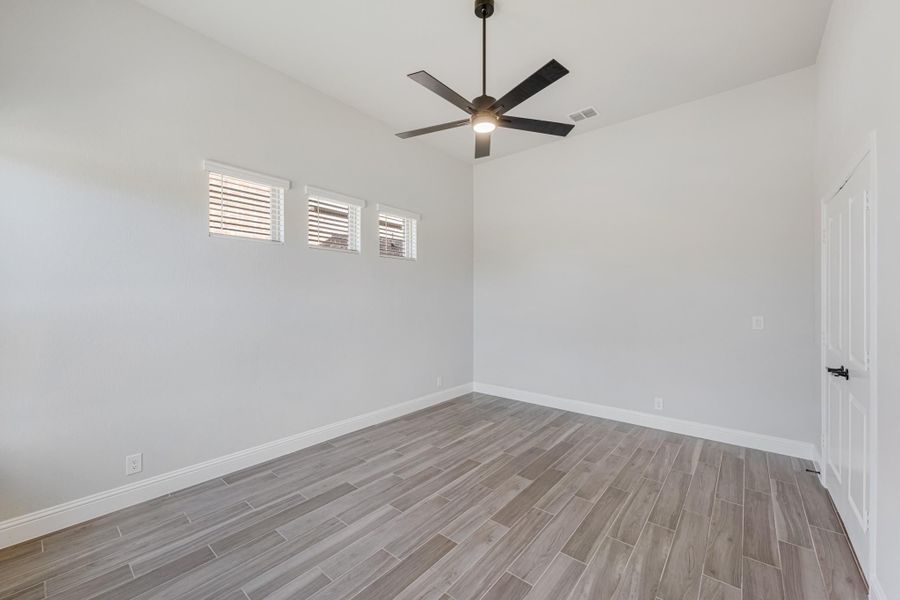Empty room with wood-look tile floors, ceiling fan, and high windows with white blinds Empty room with wood-look tile floors, ceiling fan, and high windows with white blinds