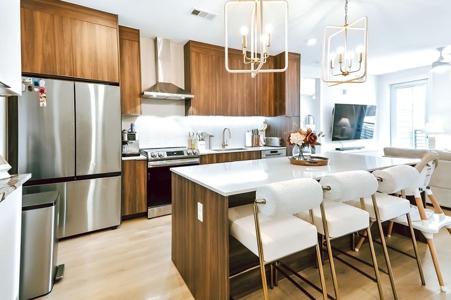 Kitchen featuring a chandelier, appliances with stainless steel finishes, wall chimney exhaust hood, a kitchen bar, and brown cabinetry