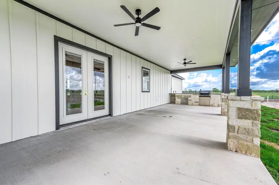 Spacious covered back patio with ceiling fans, stone accents, and an outdoor kitchen area perfect for entertaining.