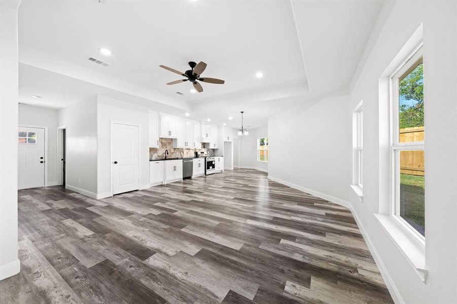 Unfurnished living room with plenty of natural light, dark wood-type flooring, a tray ceiling, a ceiling fan, and recessed lighting Unfurnished living room with plenty of natural light, dark wood-type flooring, a tray ceiling, a ceiling fan, and recessed lighting