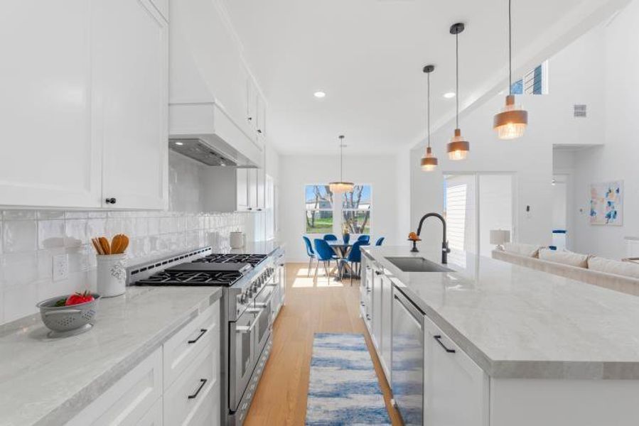 A beautifully designed kitchen featuring an undermount sink, a custom built-in microwave cabinet, concealed pull-out trash bin, brand-new dishwasher, an impressive 48-inch chef-style range, a spacious pantry, and elegant pendant lighting overhead.