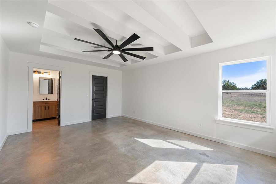 Unfurnished bedroom with finished concrete floors, a ceiling fan, ensuite bath, and a tray ceiling