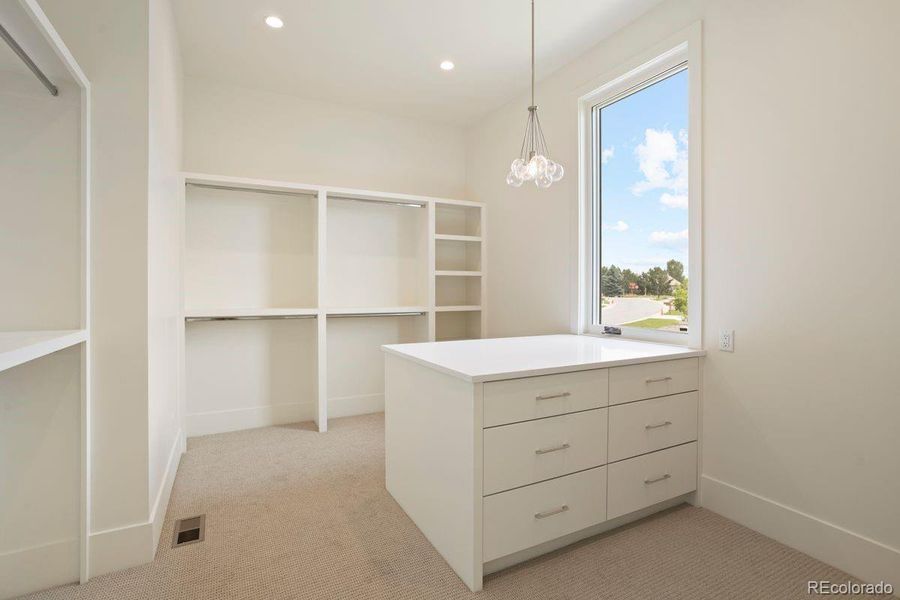 Expansive walk-in closet with custom built-ins, center island storage, and a bright window for natural light.