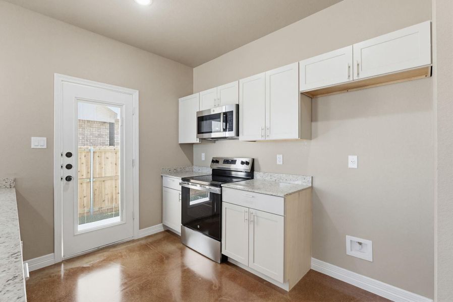 Kitchen with stainless steel appliances, concrete floors, white cabinets, and light stone counters