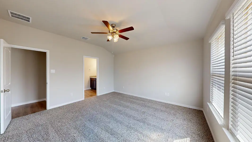 Unfurnished bedroom with light colored carpet, ensuite bathroom, lofted ceiling, ceiling fan, and multiple windows