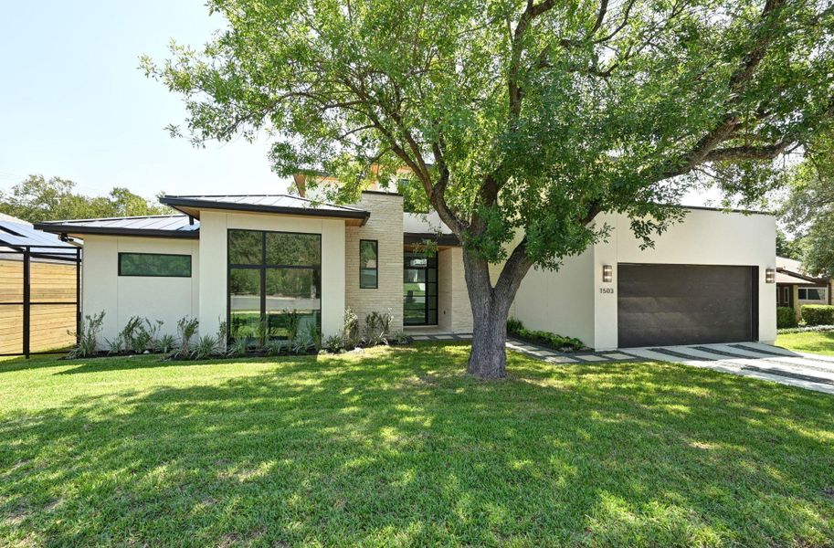 Modern home featuring a standing seam roof, a metal roof, a front yard, a garage, and stucco siding