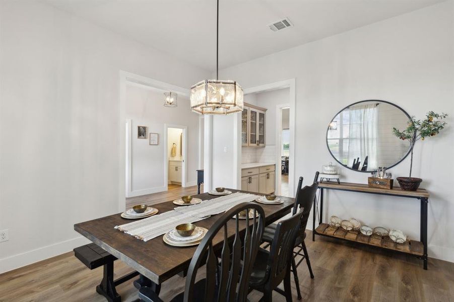 Spacious dining area featuring wood-finish flooring, a contemporary chandelier, and bright white walls