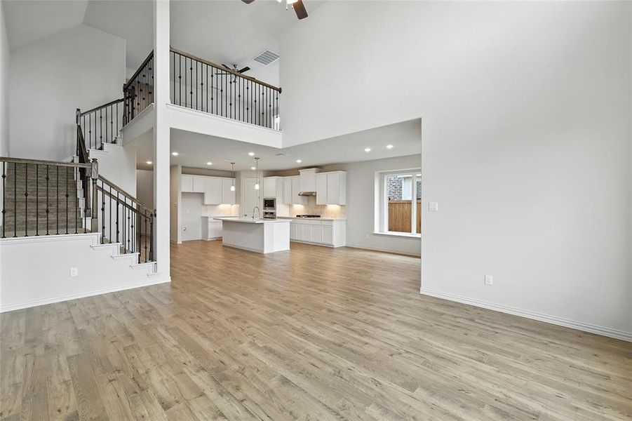 Unfurnished living room featuring light wood-type flooring, stairway, ceiling fan, and a towering ceiling