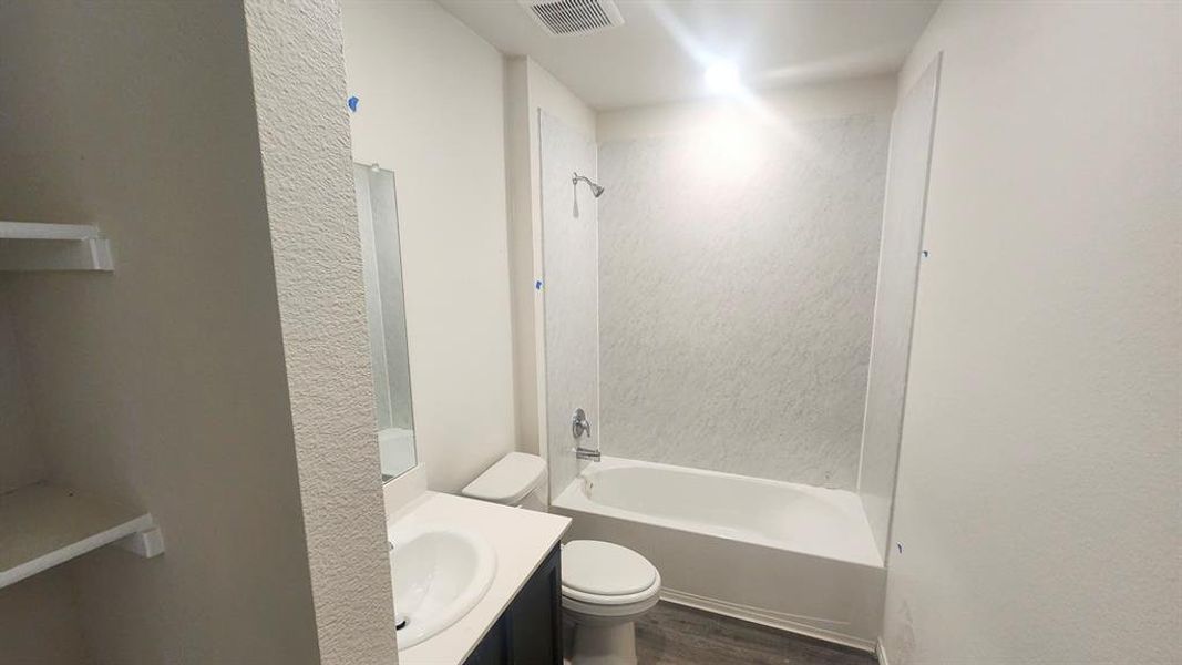 Full bathroom featuring a white porcelain tub with integrated shower, vanity with an undermount sink and dark cabinetry, a wall-mounted mirror, and wood-finish flooring