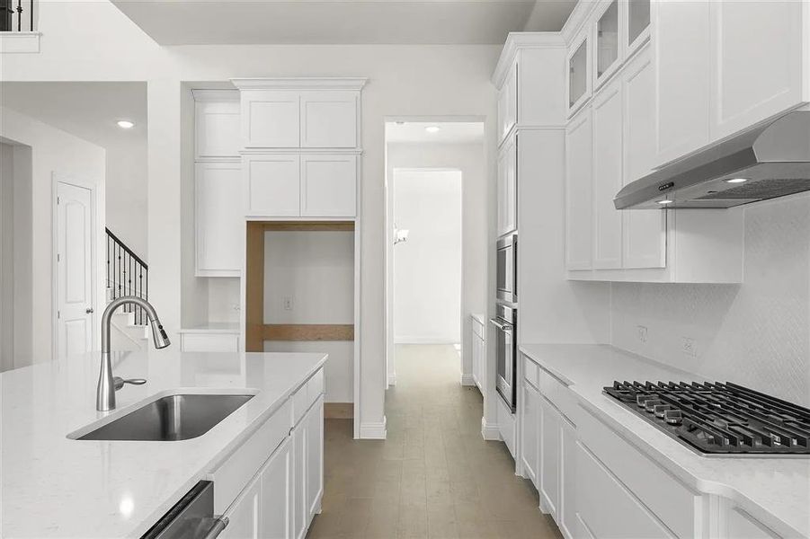 Kitchen featuring white cabinets, sink, gas stovetop, and range hood