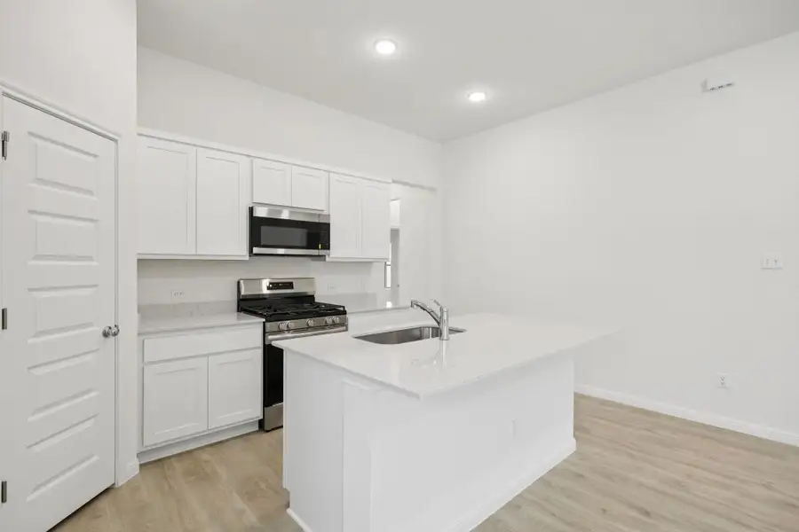 Kitchen featuring stainless steel appliances, light wood-type flooring, a kitchen island with sink, white cabinetry, and light stone countertops