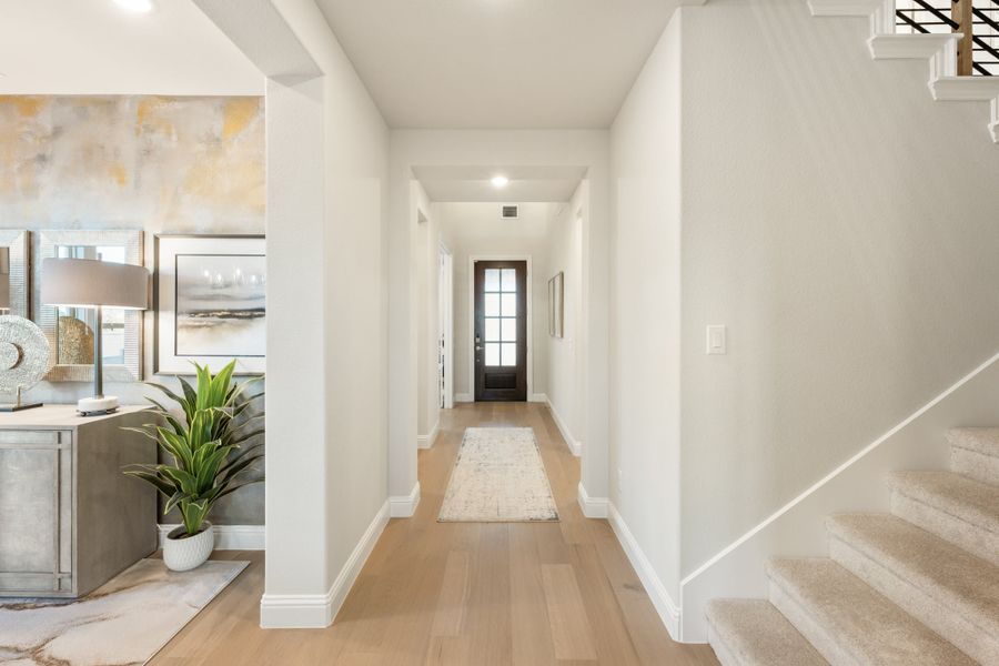 Bright entryway hallway with light wood floors, glass front door, and staircase with carpet treads