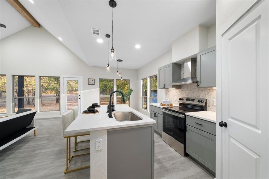 Kitchen featuring wall chimney range hood, an island with sink, gray cabinetry, sink, and electric range