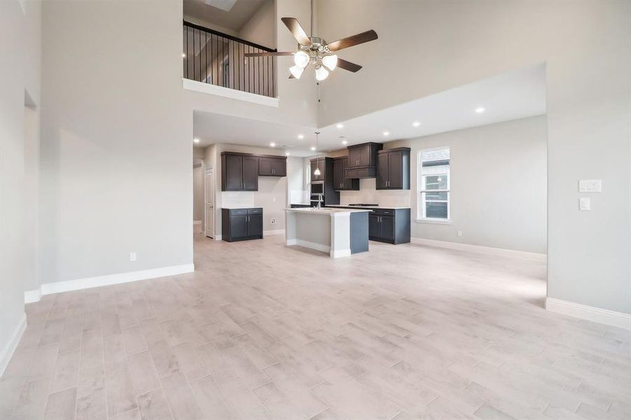 Unfurnished living room with ceiling fan, light hardwood / wood-style flooring, a high ceiling, and sink