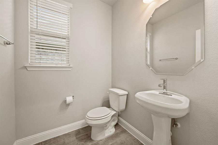 Half bath featuring a pedestal sink, updated lighting, and neutral finishes.