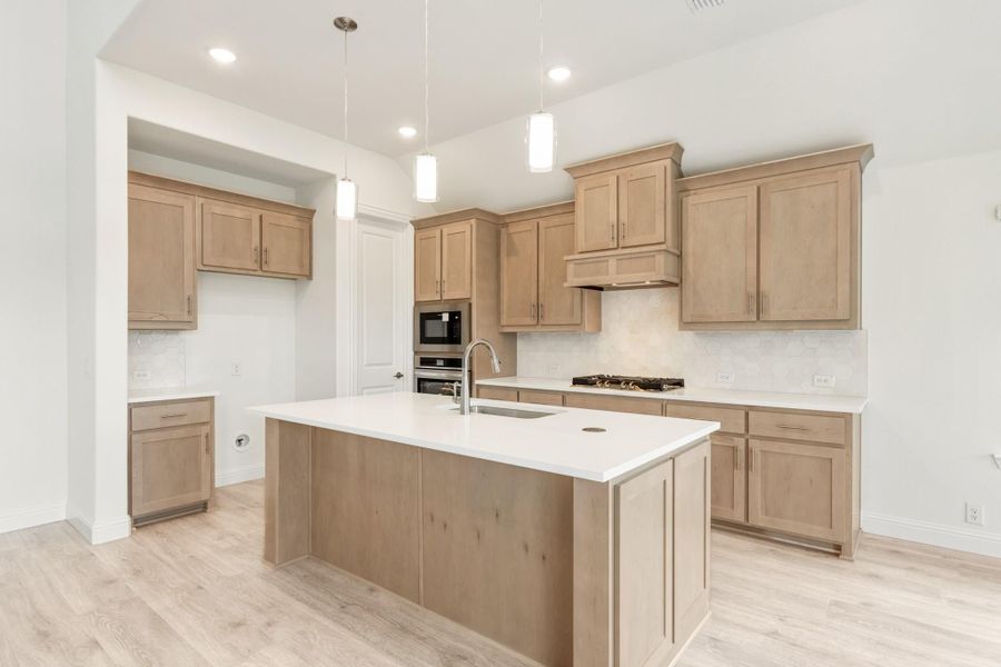 Kitchen with light wood cabinets, center island with sink, stainless steel appliances, and pendant lights over white countertops